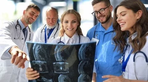 Grupo de médicos profesionales analizando radiografías de columna vertebral en un entorno clínico colaborativo. onhunters, firma de búsqueda y selección de personal.