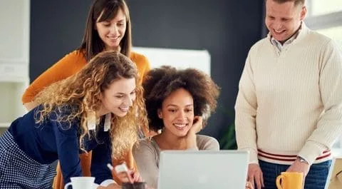 Equipo de trabajo diverso reunido alrededor de un portátil en oficina moderna, colaborando y sonriendo. onhunters, firma de búsqueda y selección de personal.
