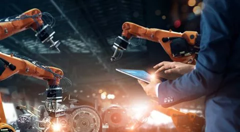 Ingeniero operando brazos robóticos industriales con una tablet en una fábrica automatizada. onhunters, firma de búsqueda y selección de personal.