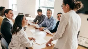 Líder femenina dirigiéndose a un grupo diverso de profesionales en una reunión de equipo colaborativa.