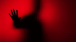 Una silueta oscura de una persona con la mano contra un fondo rojo brillante, simbolizando el "ghosting" o la desaparición en un proceso de selección.